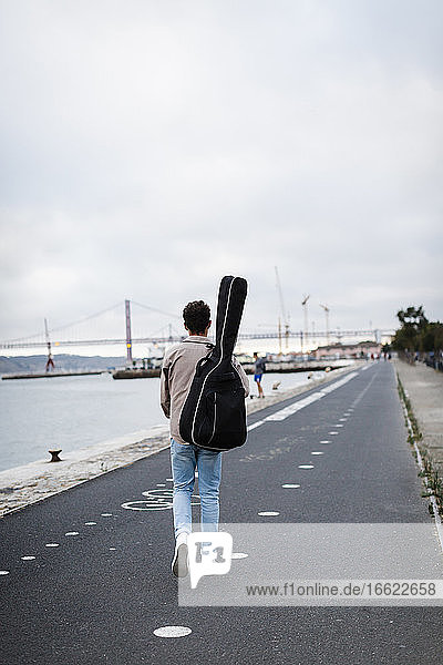 Young man with guitar walking on promenade