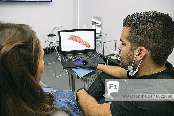 Männlicher Arzt zeigt einer Patientin ein Bild des Zahnfleisches auf einem Laptop-Bildschirm in einer Klinik