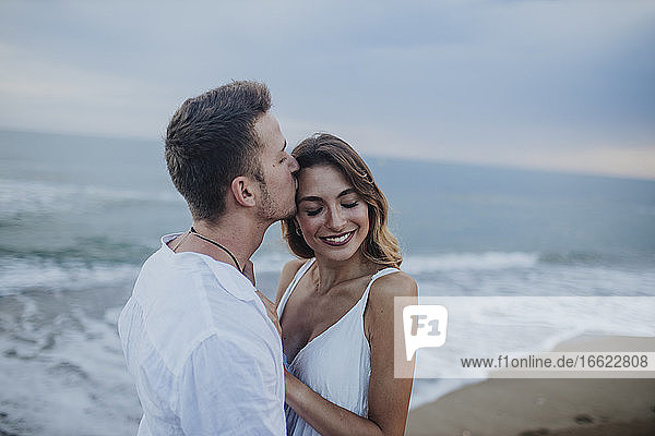 Man kissing woman while standing at beach