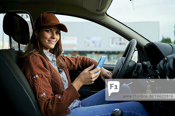 Lächelnde junge Frau  die ein Mobiltelefon benutzt  während sie im Auto sitzt