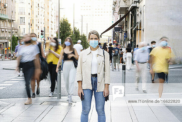 Junge Frau mit Maske steht auf der Straße in der Stadt