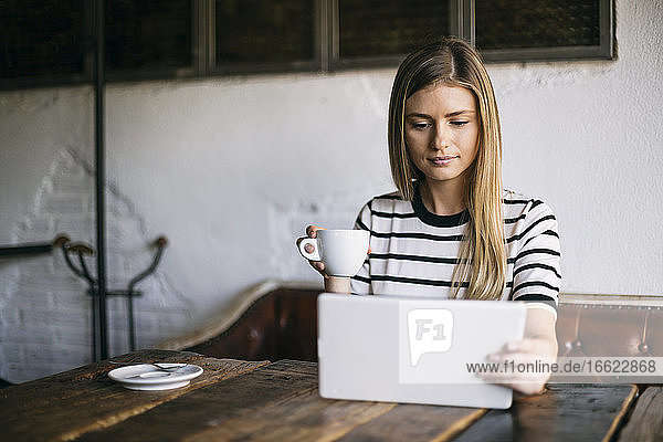 Blonde Frau  die ein digitales Tablet benutzt und Kaffee trinkt  während sie in einem Cafe sitzt