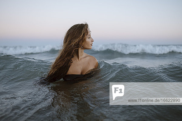 Beautiful young woman in sea at beach during sunset