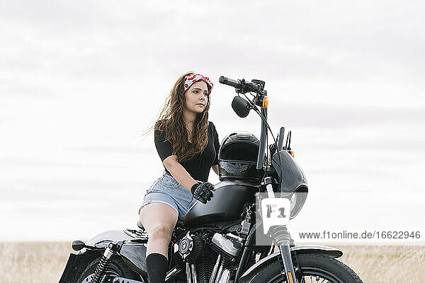Junge Frau auf Motorrad sitzend gegen den Himmel