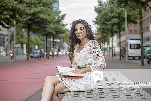 Junge Frau mit langen Haaren liest ein Buch und sitzt auf einem Sitz in der Stadt