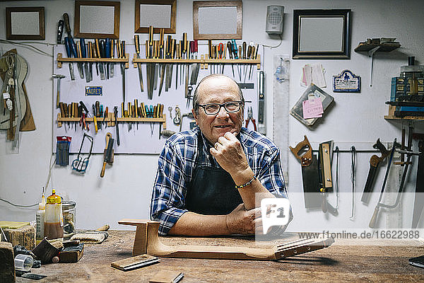 Smiling man with hand on chin standing by workbench at workshop