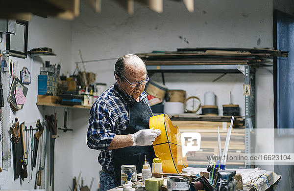 Man polishing guitar while standing by workbench at workshop