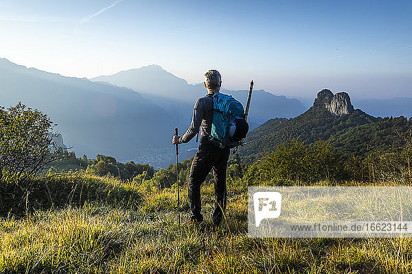 Männlicher Wanderer mit Rucksack  der bei Sonnenaufgang den Berg gegen den Himmel betrachtet  Orobie  Lecco  Italien