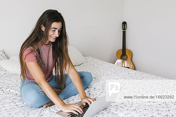 Junge Frau benutzt einen Laptop  während sie zu Hause im Schlafzimmer sitzt