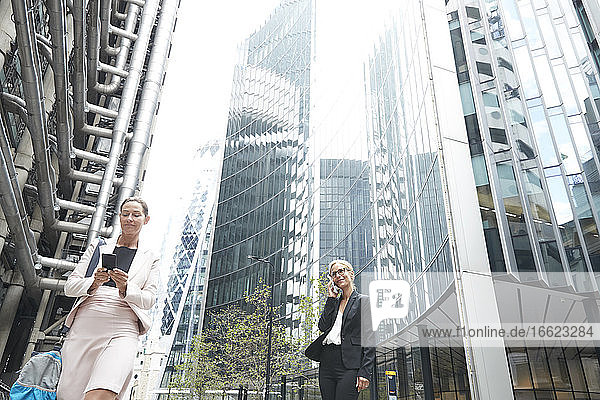 Geschäftsfrauen mit Mobiltelefonen vor Bürogebäuden in der Stadt