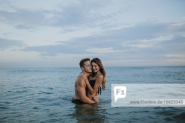Junger Mann und Frau umarmen sich gegenseitig am Strand stehend