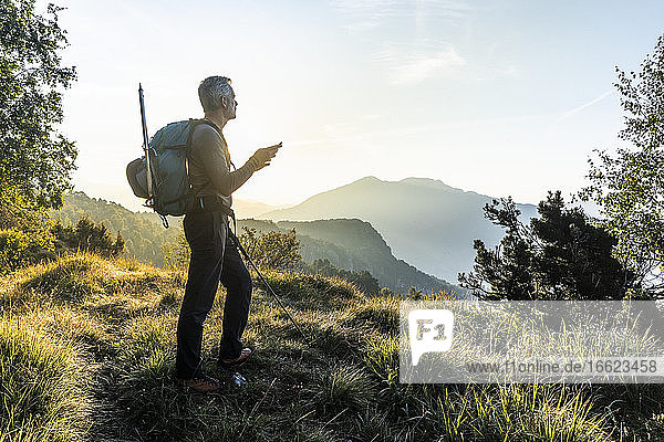 Man using mobile phone while standing on mountain against sky at sunrise  Orobie  Lecco  Italy