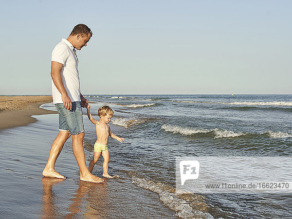Junge hält die Hand seines Vaters beim Spaziergang am Strand