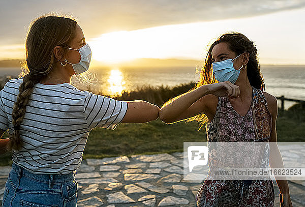 Frauen mit Gesichtsschutzmasken stoßen während des COVID-19-Ausbruchs mit dem Ellbogen gegen den Himmel