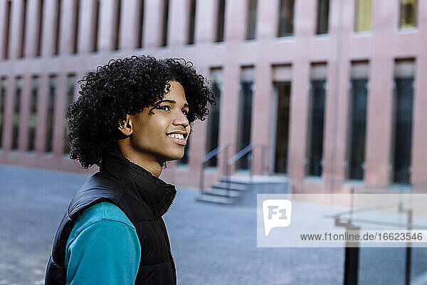 Young man looking away while standing on street in city