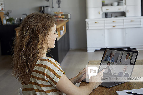 Frau  die zu Hause sitzend eine Videokonferenz über ihren Laptop abhält