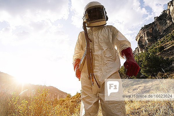 Männlicher Astronaut im Raumanzug auf einem Berg stehend gegen den Himmel an einem sonnigen Tag