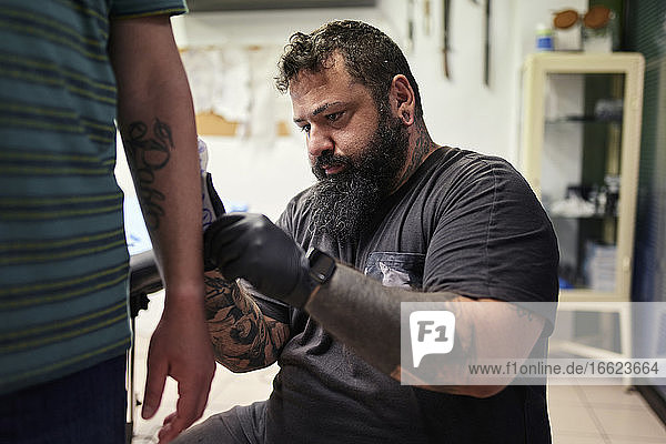 Bärtiger männlicher Künstler tätowiert in einem Studio die Hand eines Mannes