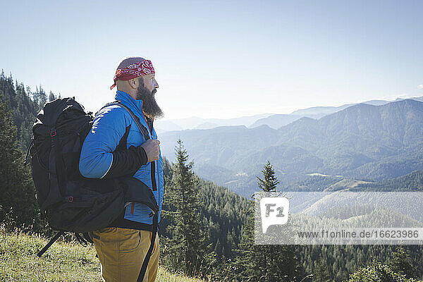 Bärtiger Mann mit Rucksack  der die Aussicht betrachtet  während er auf einem Berg gegen den klaren Himmel steht  Otscher  Österreich