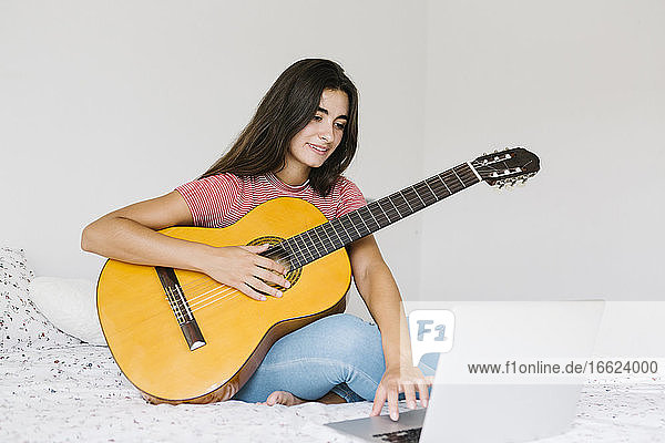 Frau lernt online zu Hause im Schlafzimmer Gitarre