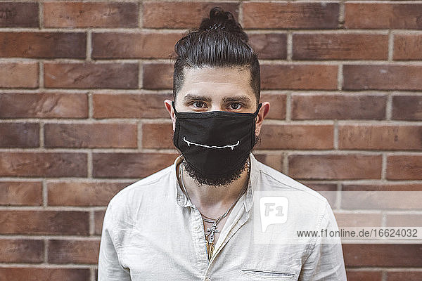 Man wearing face mask against brick wall during coronavirus crisis