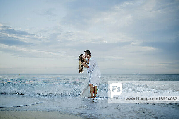 Junger Mann küsst Frau  während er am Strand im Wasser steht