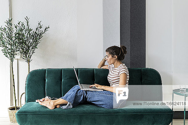 Selbstbewusste Designerin  die einen Laptop benutzt  während sie auf dem Sofa im Kreativbüro sitzt