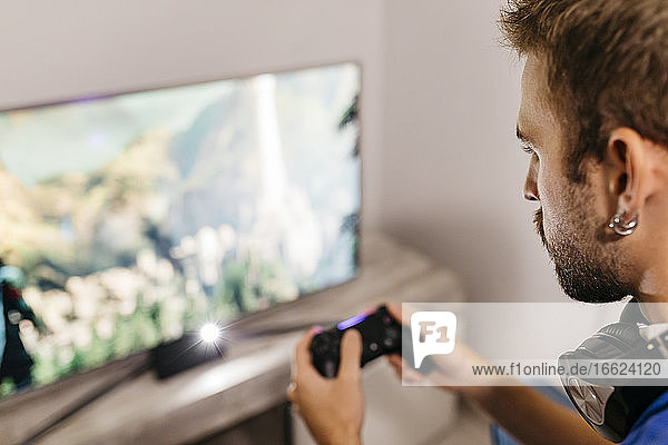 Young man holding controller while playing video game at home