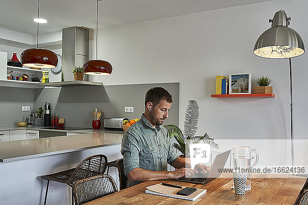 Geschäftsmann  der einen Laptop benutzt  während er am Esstisch in der Küche sitzt