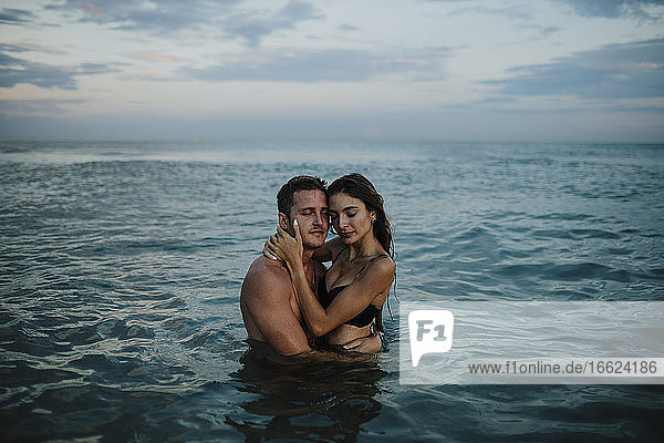 Paar mit geschlossenen Augen im Wasser stehend am Strand bei Sonnenuntergang