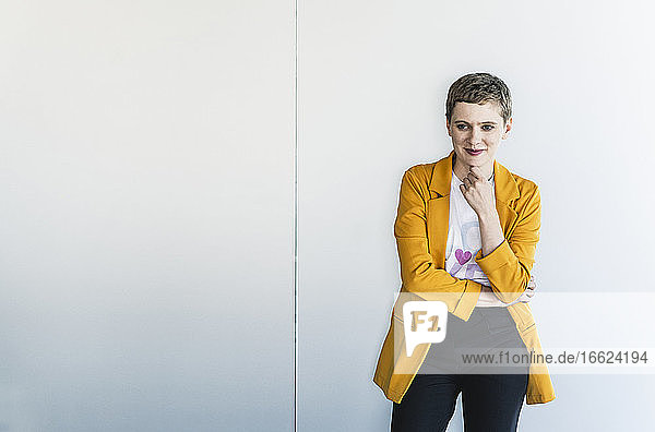 Nachdenkliche Unternehmerin mit gelbem Blazer  die im Büro an der Wand steht