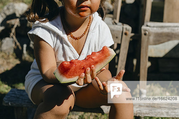 Mädchen isst Wassermelone und sitzt auf einem Baumstamm