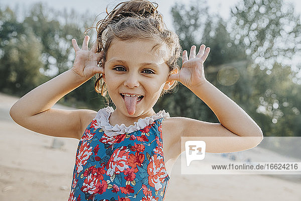 Cute little girl sticking out tongue while standing at beach