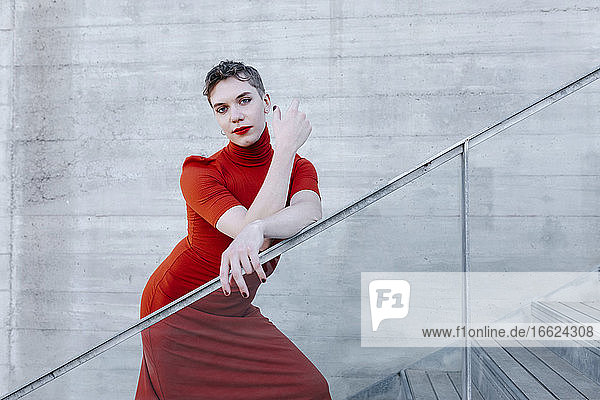Selbstbewusster Transmann in rotem Kleid steht auf einer Treppe an der Wand