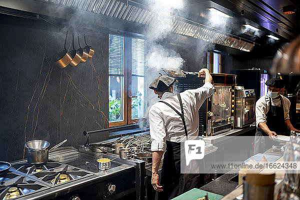 Chefs wearing protective face mask cooking dish in restaurant kitchen