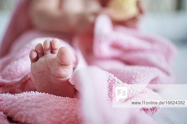 Baby girl with barefoot in pink towel on bed at home