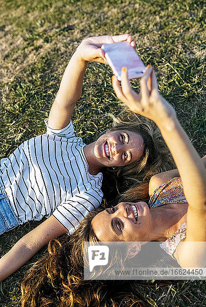 Glückliche junge Frauen  die ein Selfie machen  während sie sich auf einem Feld an einem sonnigen Tag entspannen