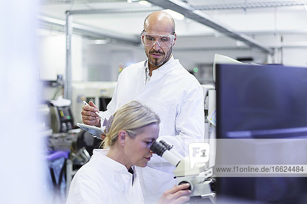 Männlicher Techniker betrachtet eine Wissenschaftlerin  die in einem Labor unter dem Mikroskop forscht