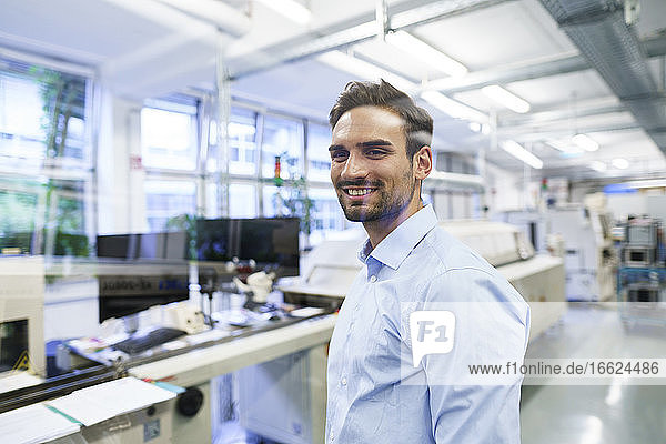 Lächelnder junger männlicher Techniker vor einer beleuchteten Fabrik