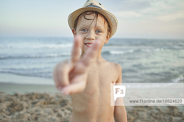 Smiling boy showing peace gesture while standing at beach