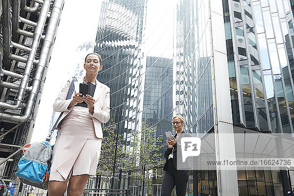 Ältere Geschäftsfrauen mit Smartphones vor einem modernen Bürogebäude in der Innenstadt