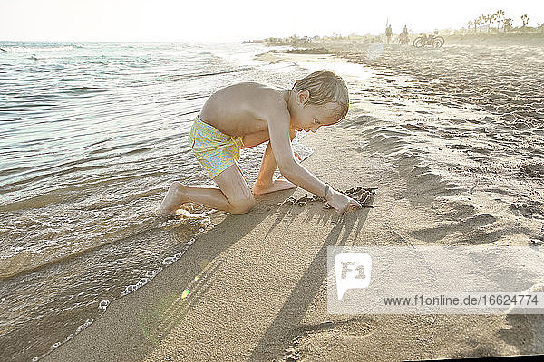 Boy sitting and playing in sand at beach