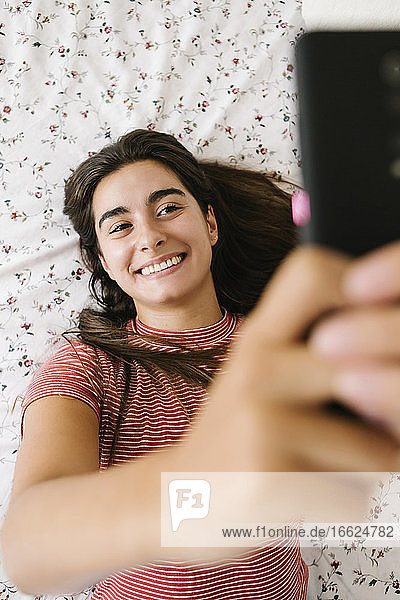 Smiling woman taking selfie on smart phone in bedroom