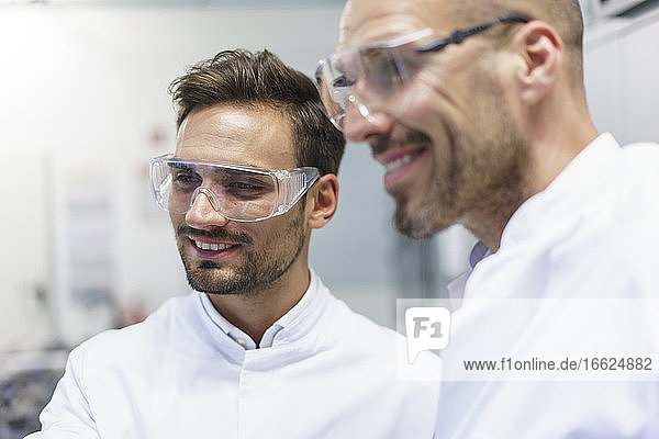 Smiling male technicians looking away at illuminated laboratory