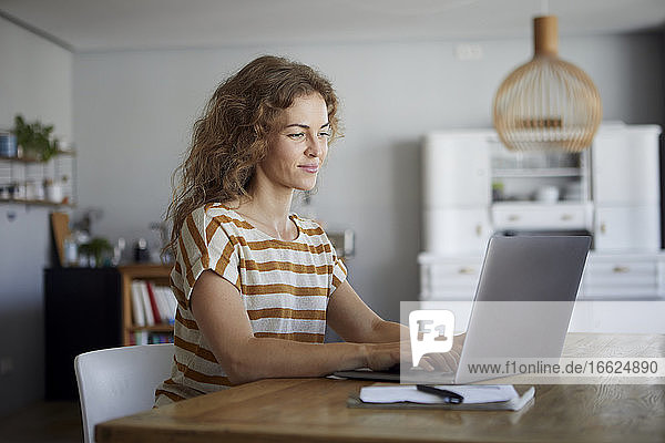 Mid adult woman working on laptop while sitting by table at home