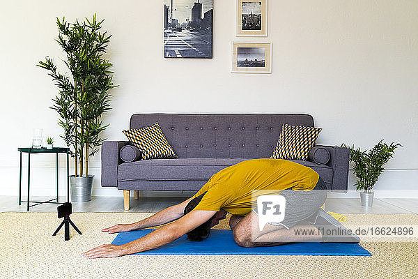 Fitnesstrainer mit Stativ und Mobiltelefon kniend beim Training zu Hause