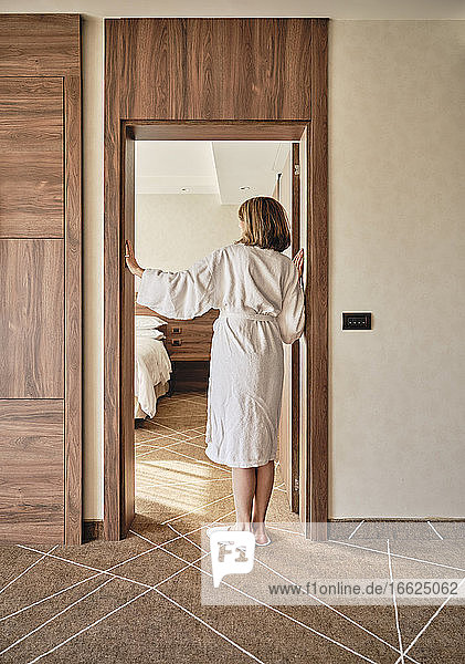 Senior woman in bathrobe standing at hotel room doorway
