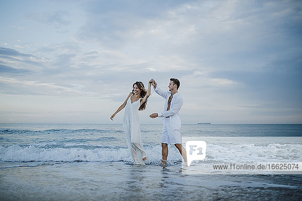 Junges Paar  das eine Frau beim Tanzen im Wasser am Strand dreht