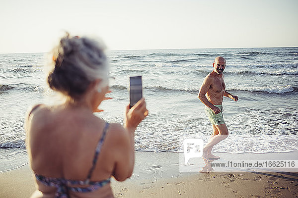 Frau fotografiert Mann beim Laufen am Strand