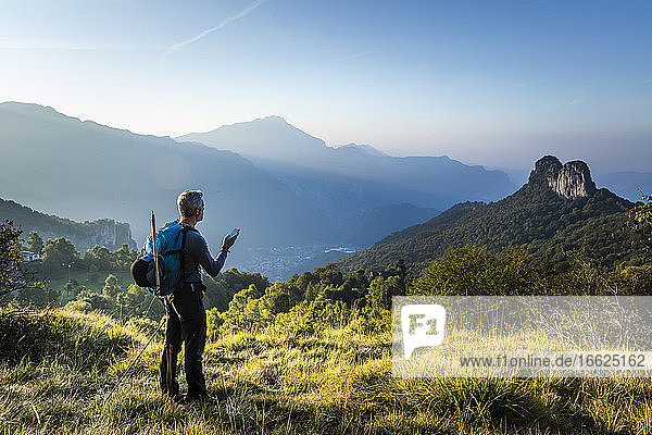 Man with backpack using mobile phone standing on mountain during sunrise  Orobie  Lecco  Italy